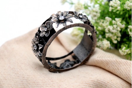 Pulseira em prata recortada, tipo escrava, com aplicações florais,  pedras em talhe brilhante e corrente de segurança.