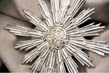 Resplendor de prata relevada com motivos florais no centro.