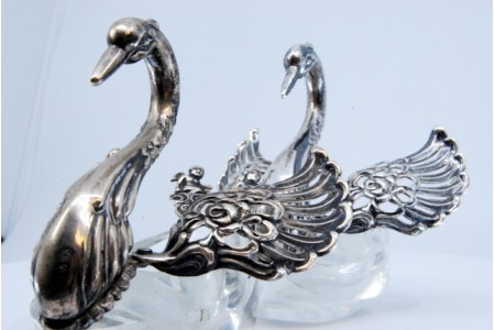 Saleiro e pimenteiro em vidro com figuras de cisnes de asas abertas em prata.
