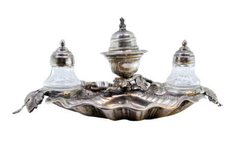 Tinteiro em prata com dois depósitos em vidro lapidado e campainha, cartela para monograma e assente sobre três pés em forma de folhas de acanto.