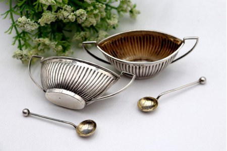 Conjunto de saleiro e pimenteiro em forma de navete com duas colheres.