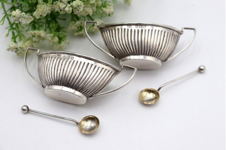 Conjunto de saleiro e pimenteiro em forma de navete com duas colheres.