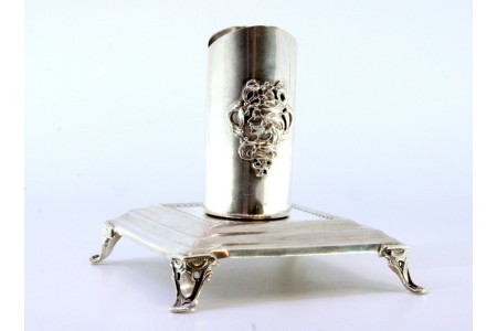 Suporte em prata para vela com figura de jovem relevada e assente em base quadrada com quatro pés recortados.