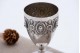 Taça de prata com rostos relevados e base circular.