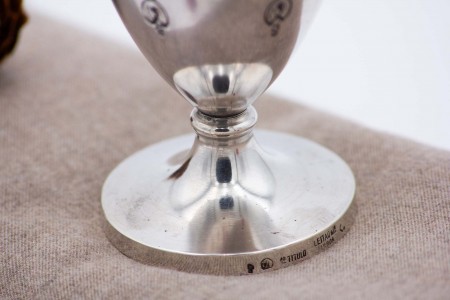 Taça de prata com rostos relevados e base circular.