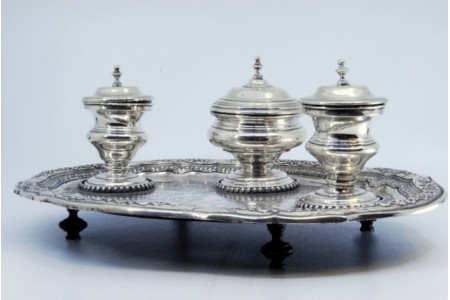 Tinteiro em prata com três recipientes gravados, campainha, suporte de canetas e bandeja assente sobre quatro pés com garras.