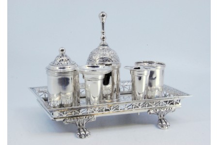 Tinteiro em prata com gradinha recortada, dois suportes para canetas, campainha, tinteiro, areeiro e assente em quatro pés em forma de garras.