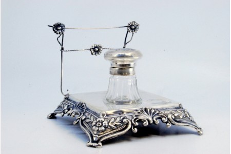 Tinteiro em prata com relevos florais, depósito em vidro lapidado e assente em quatro pés.