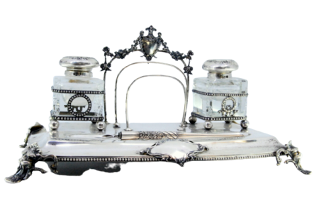 Tinteiro em prata com dois depósitos em vidro, caneta, suporte para cartas e assente sobre quatro pés de mascarões. 