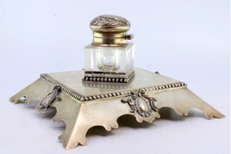 Tinteiro com base em prata perlada na envolvência com laços e brasões com depósito em vidro e tampa articulada.