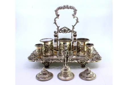 Tinteiro em prata cinzelada, bandeja recortada com três depósitos, porta canetas, campainha e assente sobre quatro pés relevados com garras.