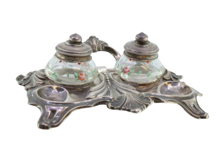 Tinteiro em prata relevada com dois depósitos em vidro pintados com motivos florais e assente sobre quatro pés recortados.