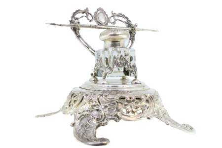 Tinteiro em prata recortada com depósito em vidro, suporte para canetas e assente sobre quatro pés relevados.