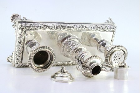 Tinteiro em prata com relevos e aplicações, dois depósitos, porta canetas e assente em quatro pés recortados.