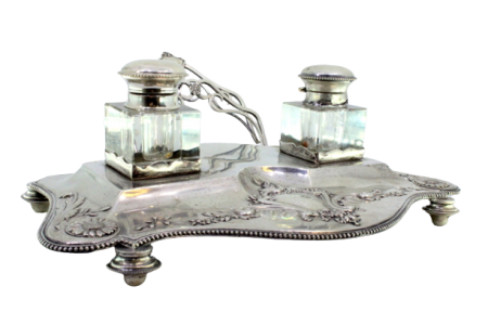 Tinteiro em prata com motivos florais relevados e envolvendo cartela para monograma, dois depósitos em vidro, porta cartas, friso perlado e assente em quatro pés redondos.