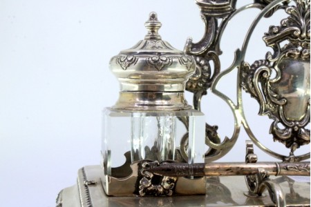 Tinteiro em prata recortada com dois depósitos em vidro, porta cartas, porta canetas, com cartelas para monogramas, assente em quatro pés relevados, friso perlado e base forrada a madeira.