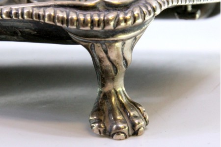 Tinteiro em prata com gradinha nos três depósitos em vidro com frisos envolventes e assente em quatro pés em forma de garras.