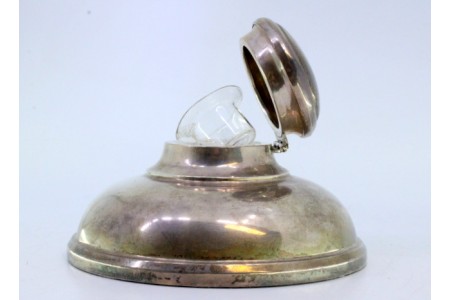 Tinteiro em prata lisa de forma redonda com depósito em vidro no interior e base preenchida.