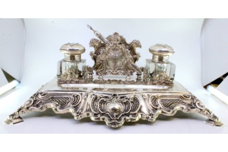 Tinteiro em prata recortada com relevos concheados, dois depósitos em vidro, suporte para cartas, caneta e assente em quatro pés.