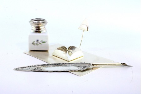 Tinteiro em prata com depósito em cerâmica, base fosqueada, suporte e pena para escrita.