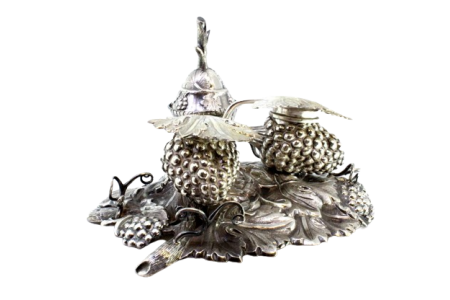 Tinteiro em prata com relevos em forma de cachos uvas e parras, campainha, areeiro, suportes para penas e tampas basculantes.