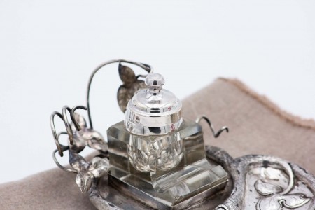 Tinteiro de prata com um depósito de vidro, folhas de acanteiro relevadas e assente em três pés.