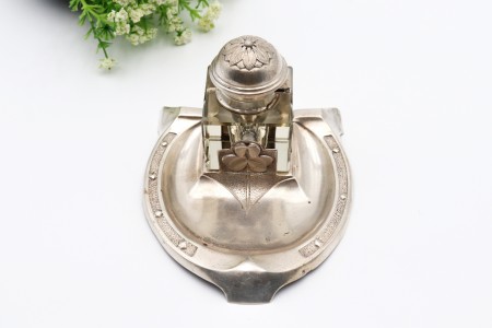 Tinteiro com estrutura em prata relevada em forma de ferradura e um depósito em vidro com tampa em alto relevo