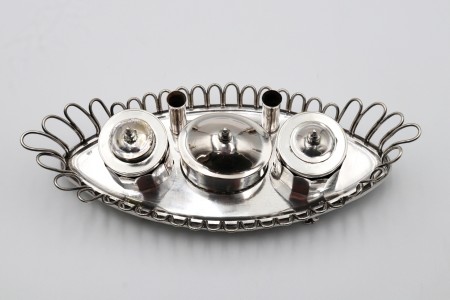  Tinteiro em prata com estrutura aramada em forma de nave, depósitos em vidro e suporte para canetas com assente em quatro pés recortados.