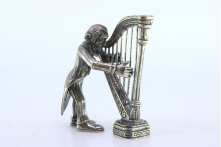 Figura de músico em prata tocando harpa.