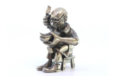 Figura de sapateiro em prata sentado reparando o calçado.