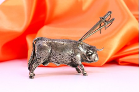 Touro em prata com figura profusamente definida e quatro espadas no dorso.