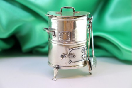 Churrasqueira de prata em miniatura com relevos e aplicações, vários utensílios e porta basculante.