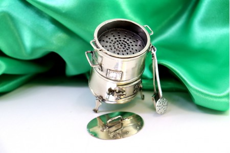 Churrasqueira de prata em miniatura com relevos e aplicações, vários utensílios e porta basculante.